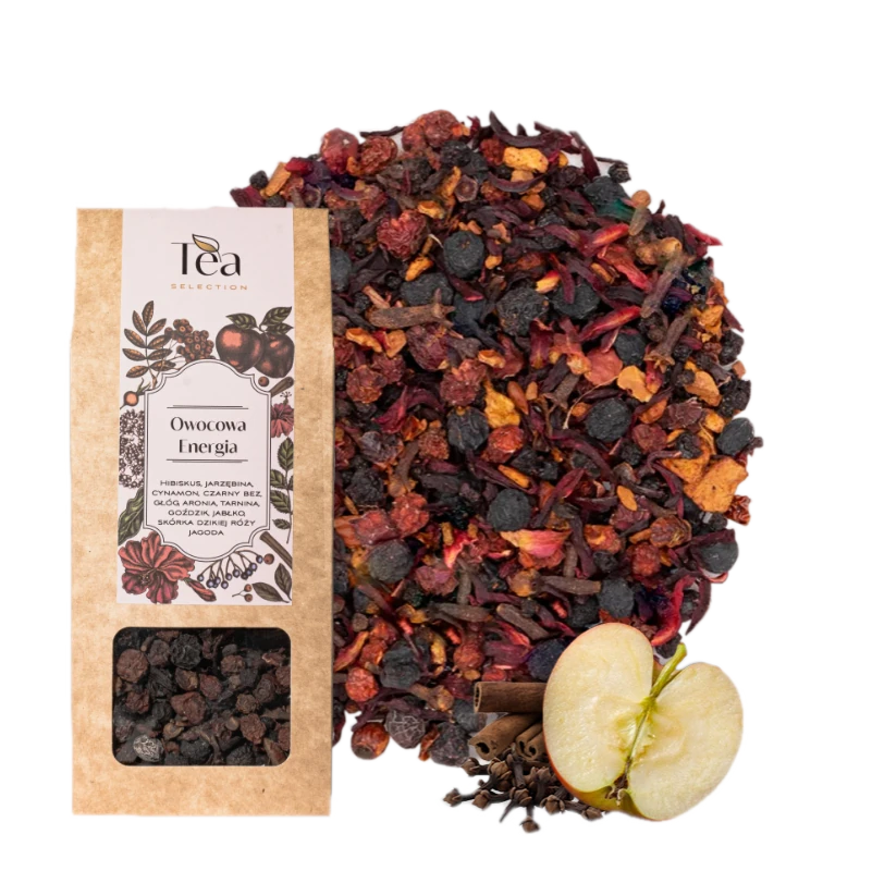 Opakowanie herbaty Owocowa Energia na białym tle, zawierającej mieszankę hibiskusa, jarzębiny, cynamonu, czarnego bzu, głogu, aronii, tarniny, goździków, jabłka, skórki dzikiej róży i jałowca, obok talerz z suszonymi owocami i przyprawami, pół jabłka, laska cynamonu oraz goździki