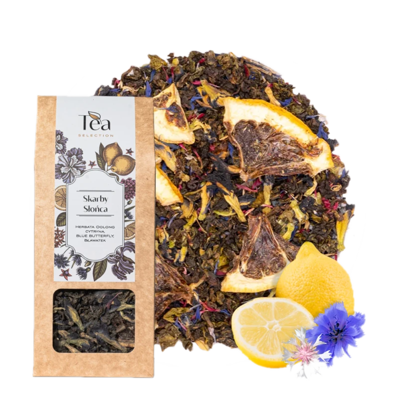 Opakowanie herbaty Skarby Słońca na białym tle, zawierającej mieszankę herbaty oolong, cytryny, blue butterfly oraz bławatera, obok talerz z suszonymi owocami i kwiatami, połowa cytryny, całe cytryny oraz niebieskie kwiaty chabra i białe kwiaty bławatera