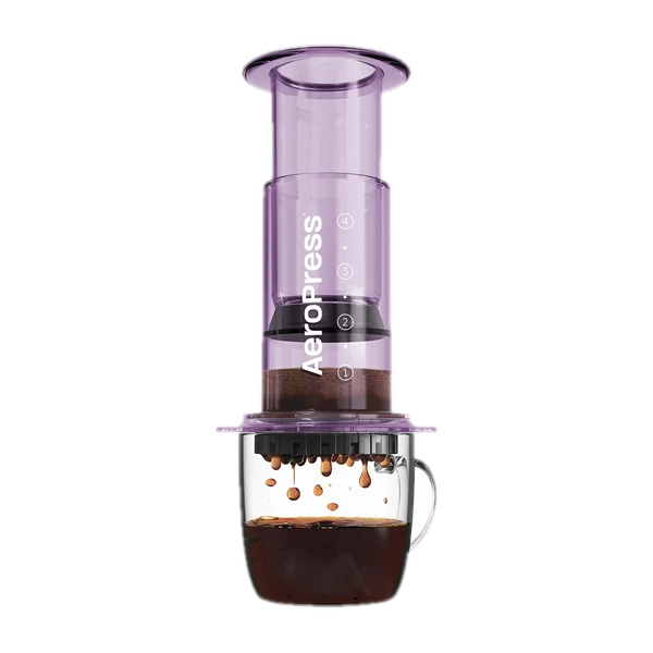 Zdjęcie fioletowego zaparzacza AeroPress Clear Purple, umieszczonego na szklance z zaparzaną kawą. Krople kawy spadają do kubka, ukazując proces parzenia metodą AeroPress, z przezroczystym fioletowym korpusem urządzenia.