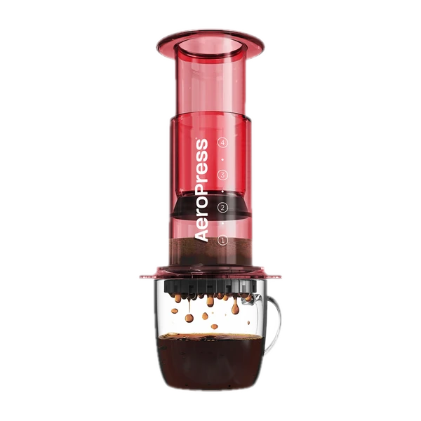 Zdjęcie czerwonego zaparzacza AeroPress Clear Red, umieszczonego na szklance z zaparzaną kawą. Krople kawy spadają do kubka, pokazując proces parzenia metodą AeroPress, z przezroczystym czerwonym korpusem urządzenia.